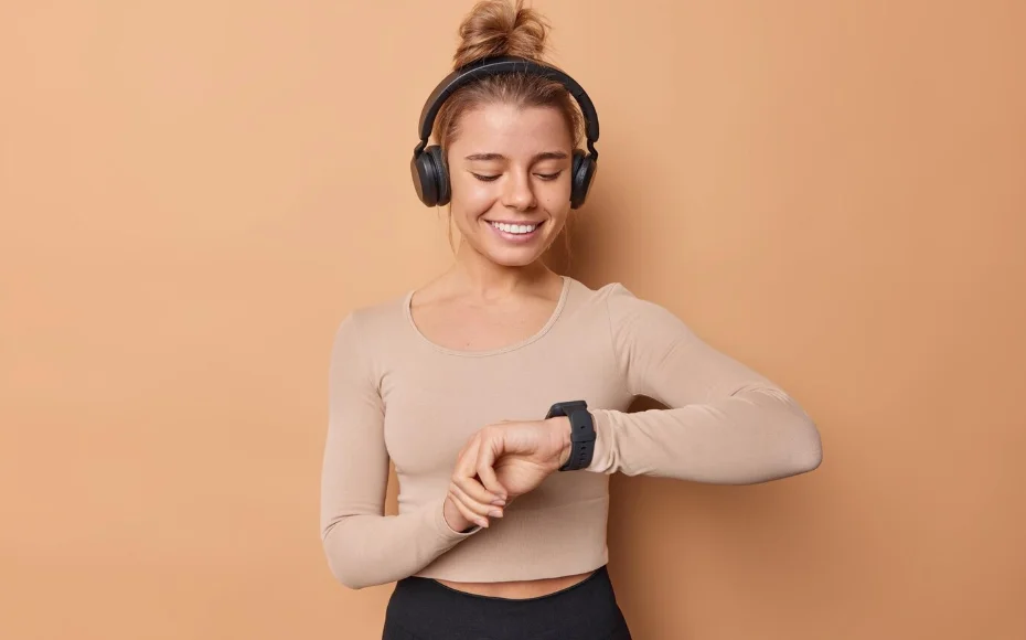 Mujer sonriendo, utilizando su smartwatch para cambiar la música de sus auriculares inalámbricos