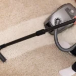 Persona limpiando con la aspiradora la alfombra de casa como parte de la limpieza del hogar