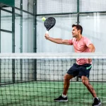 Deportista jugando al pádel, golpeando una pelota con su pala mientras se encuentra en un punto activo del juego.