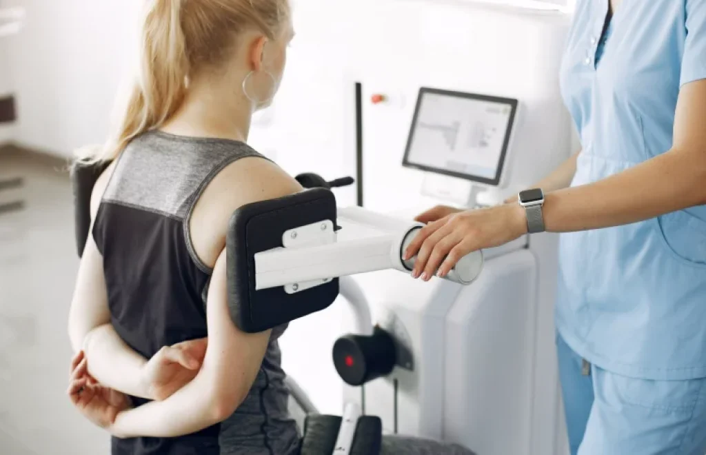 Paciente recibiendo tratamiento de rehabilitación en el brazo con un equipo de fisioterapia avanzada bajo la supervisión de un profesional.