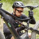 Ciclista revisando la suspensión y la batería de una bicicleta eléctrica de montaña (e-bike) durante una ruta, tecnología aplicada al deporte cotidiano