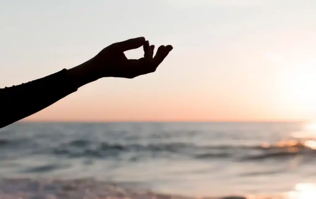 Persona meditando frente al mar al atardecer como parte de planes para desconectar y reconectar con el bienestar