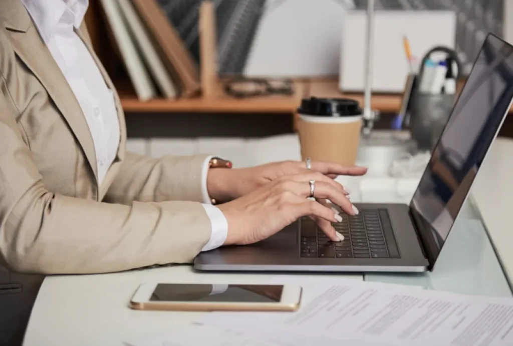 Persona realizando trámites online desde un portátil en un escritorio con documentos y móvil