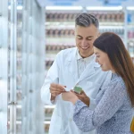 Farmacéutico atendiendo a una clienta en una farmacia y explicándole un producto