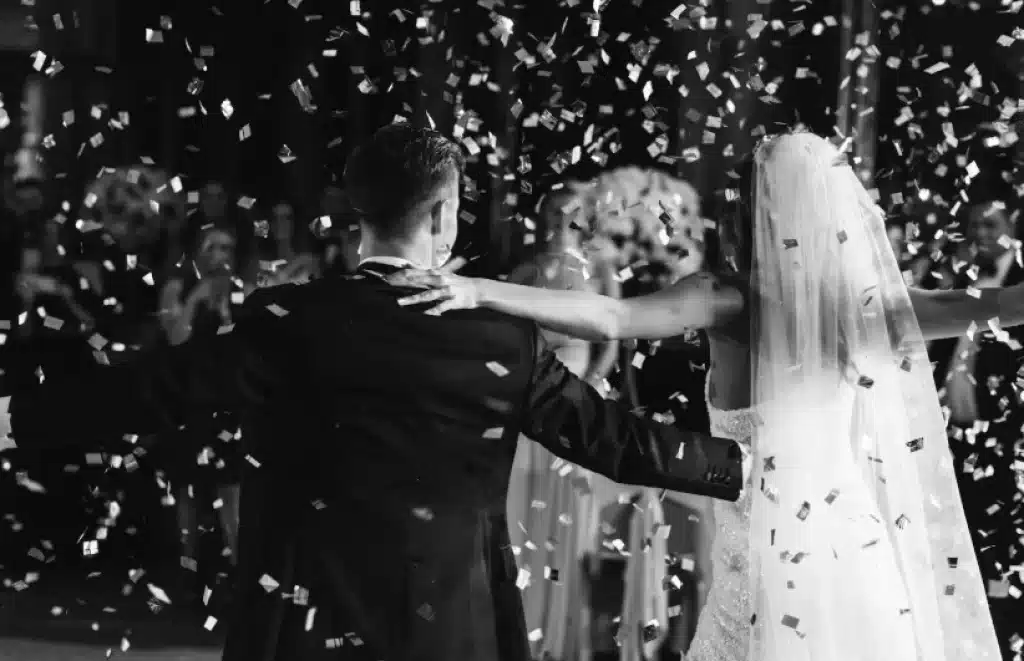 Novios bailando durante su boda bajo una lluvia de confeti en una celebración elegante en blanco y negro