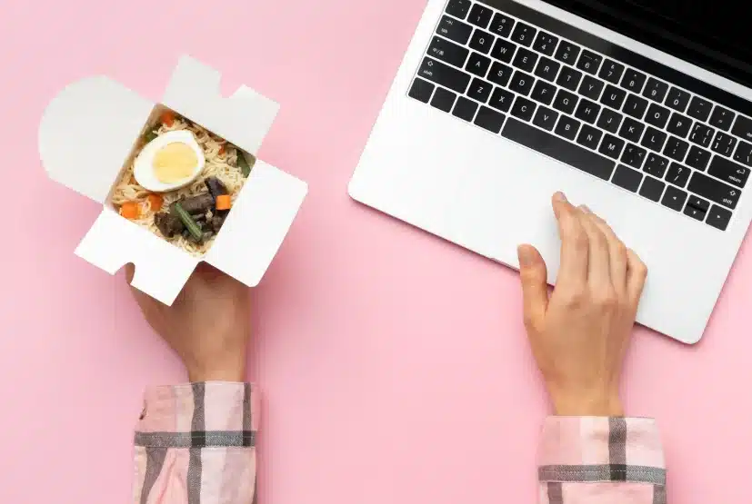 Persona usando un portátil mientras sostiene un envase de comida, representando la compra de comida online
