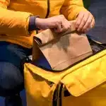 Repartidor guardando una bolsa de comida para llevar en una mochila térmica amarilla de delivery