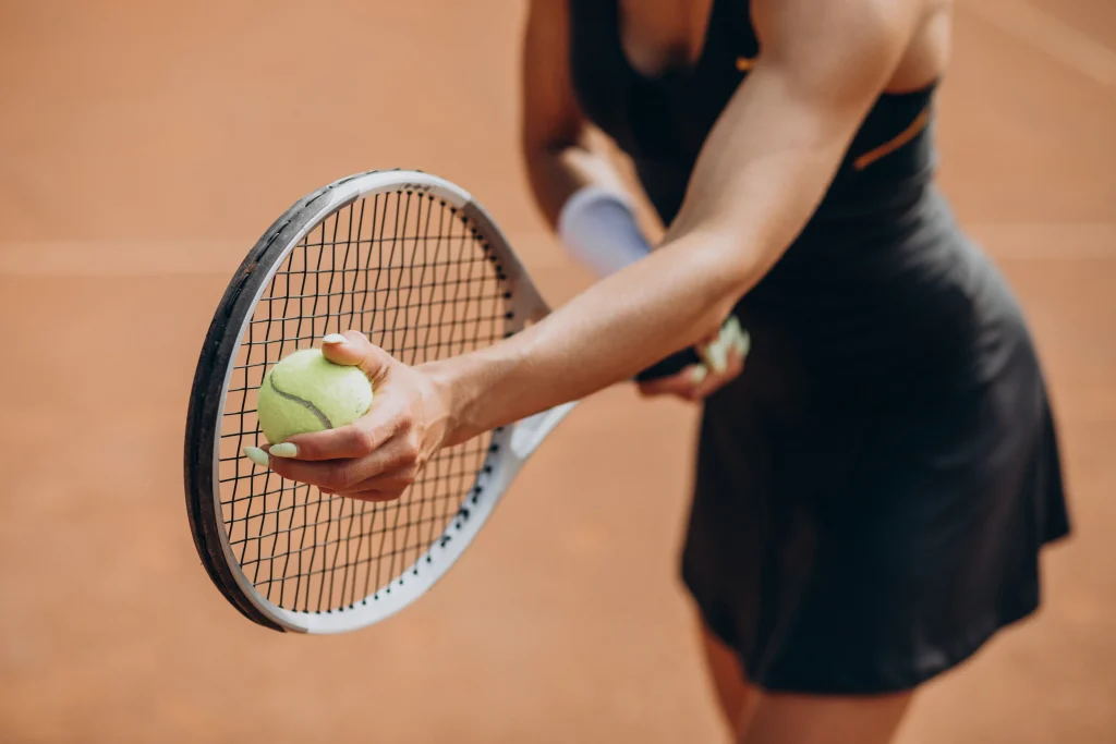 Jugadora de tenis sujetando una pelota junto a la raqueta en una pista de tierra batida